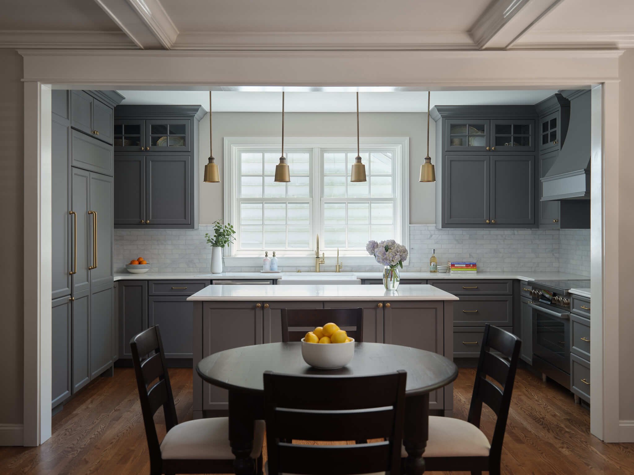 Kitchen with gray cabinets, white marble countertops, a window above the sink, a round dining table with a bowl of lemons, pendant lights, and hardwood floors.