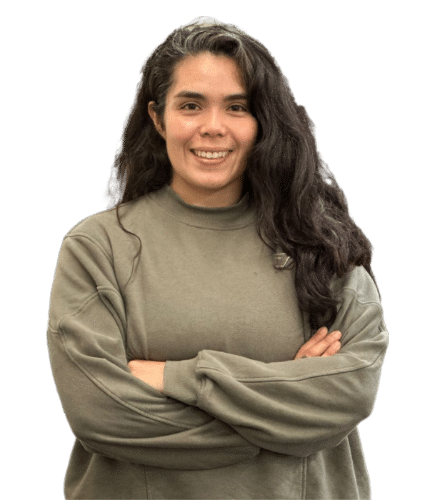 A young woman with long, dark, curly hair, smiling, wearing a beige sweatshirt with her arms crossed.