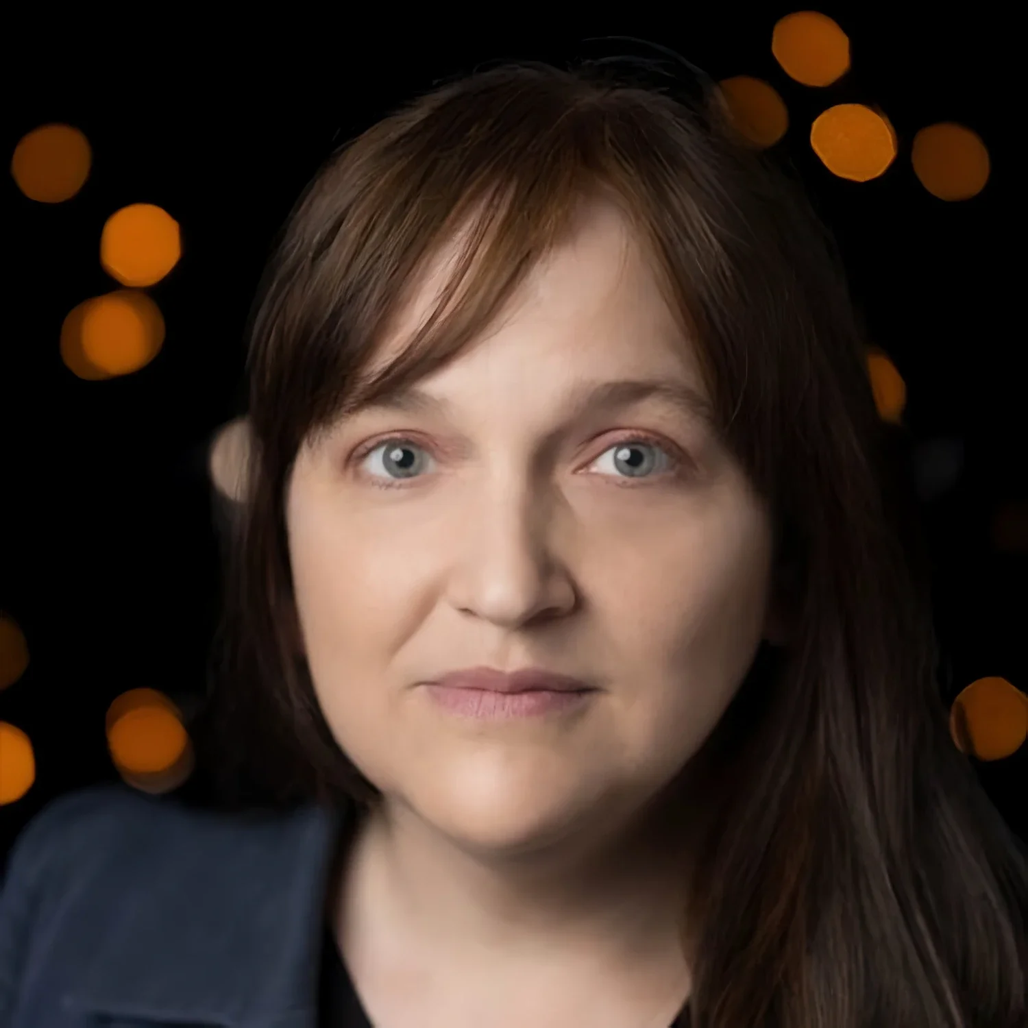 A smiling woman with short red hair wearing a yellow patterned scarf and a black top.