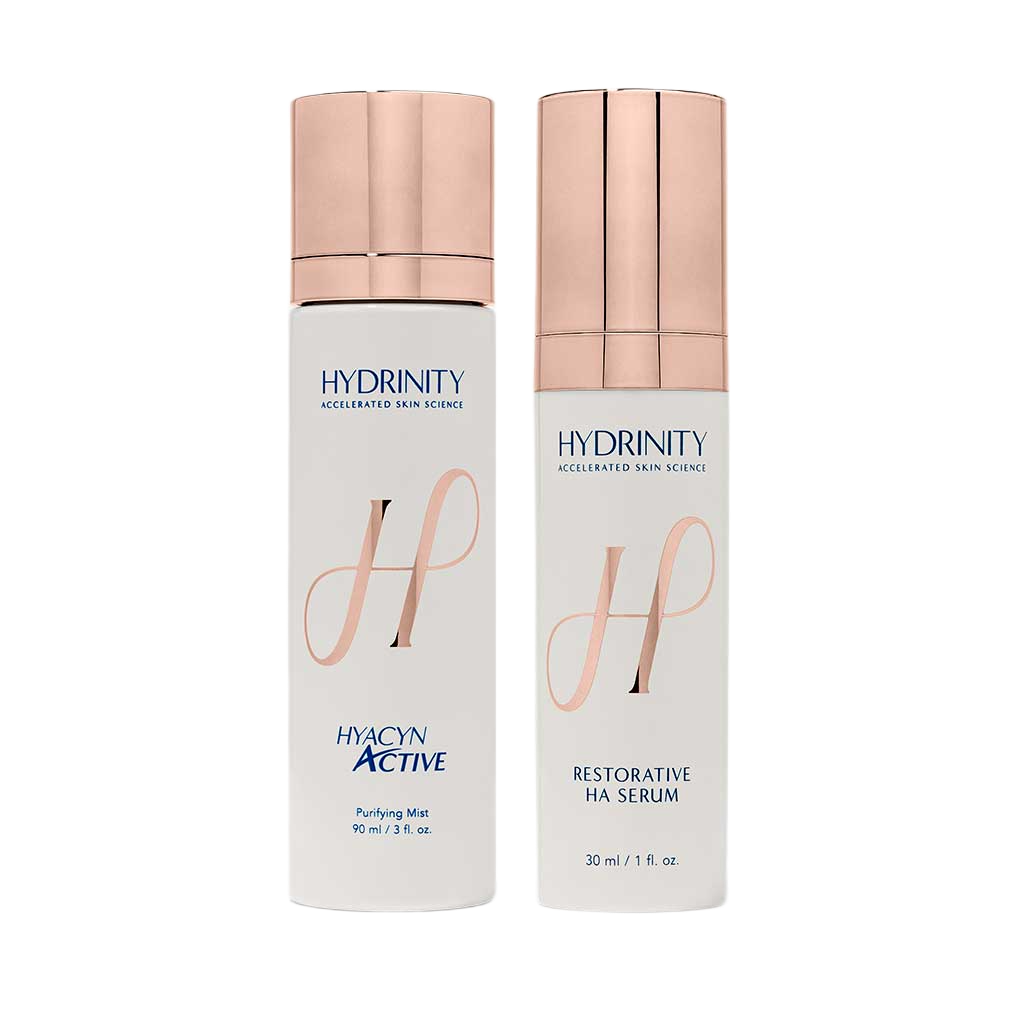 Two skincare product bottles from Hydrinity, one labeled Hydacyn Active Purifying Mist and the other labeled Restorative HA Serum, with pink caps and white bottles.