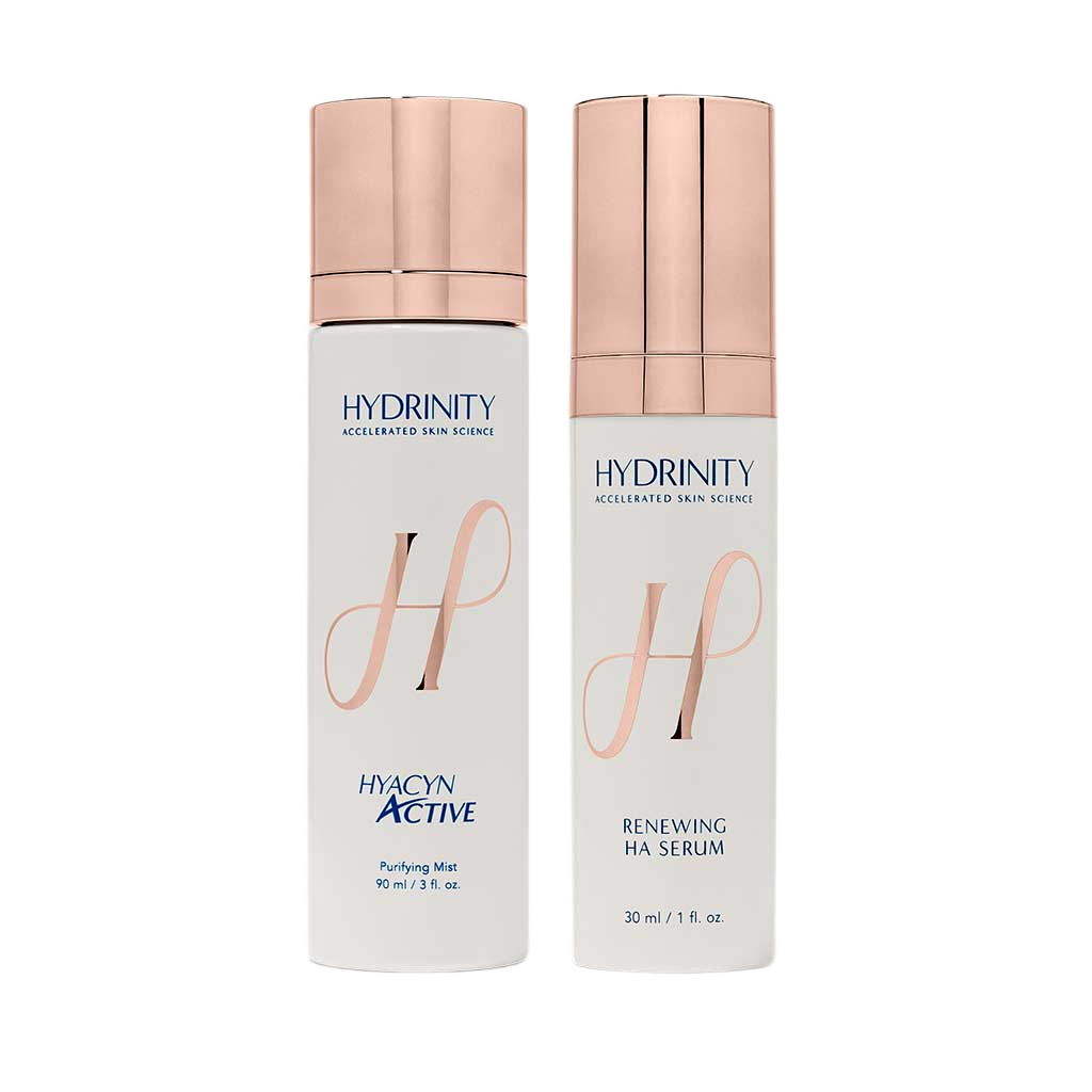 Two bottles of Hydrinity skincare products, one labeled Hydacyn Active Purifying Mist and the other Hydrinity Renewing HA Serum, with light pink metallic caps and white bodies.
