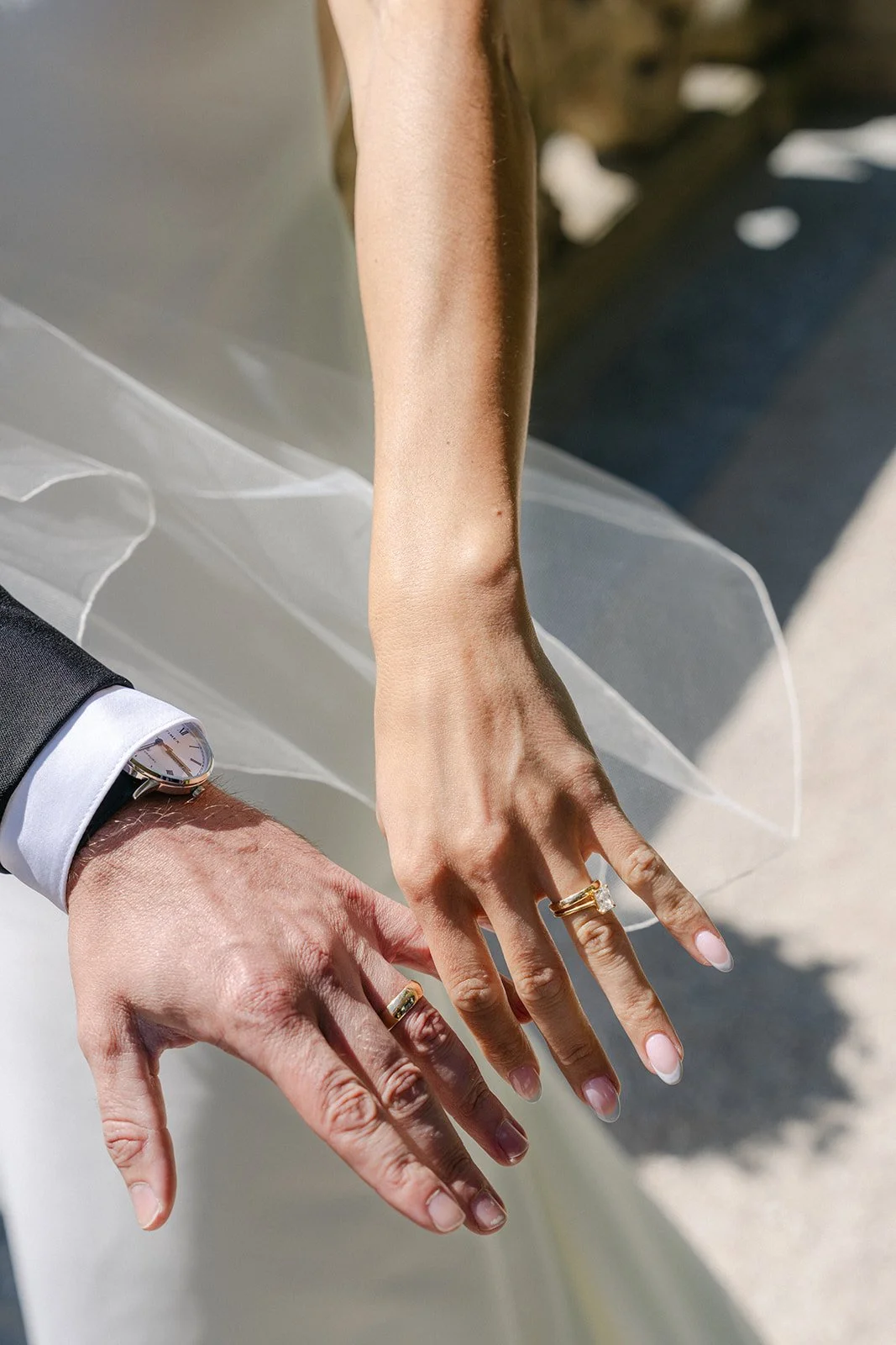 Close-up of a couple's hands displaying wedding rings, with the woman's hand on top and the man's hand with a watch underneath.