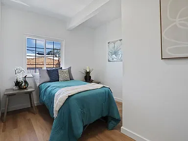 A bedroom with a bed covered in teal bedding, two windows, and minimal decor.