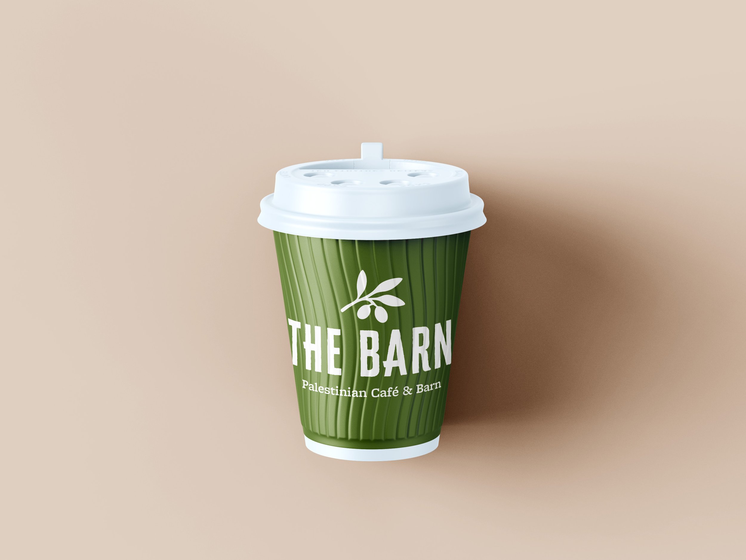 A green disposable coffee cup with a white lid and logo for 'The Barn Palestinian Cafe & Barn' on a beige background.