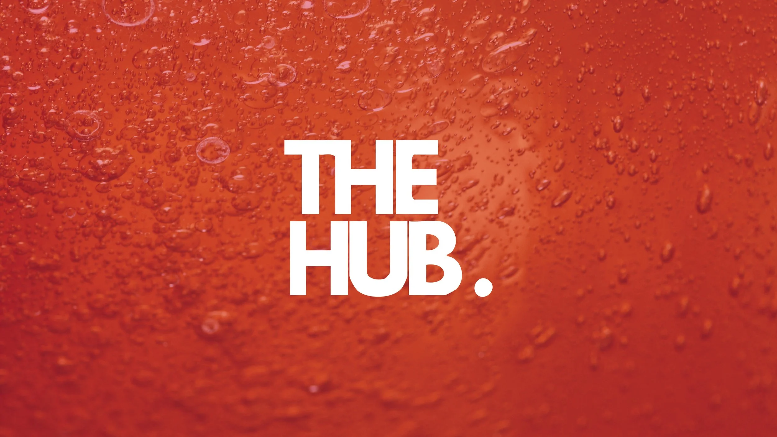 Close-up of a dark red beverage with bubbles, with the text 'THE HUB.' in white, bold font in the center.