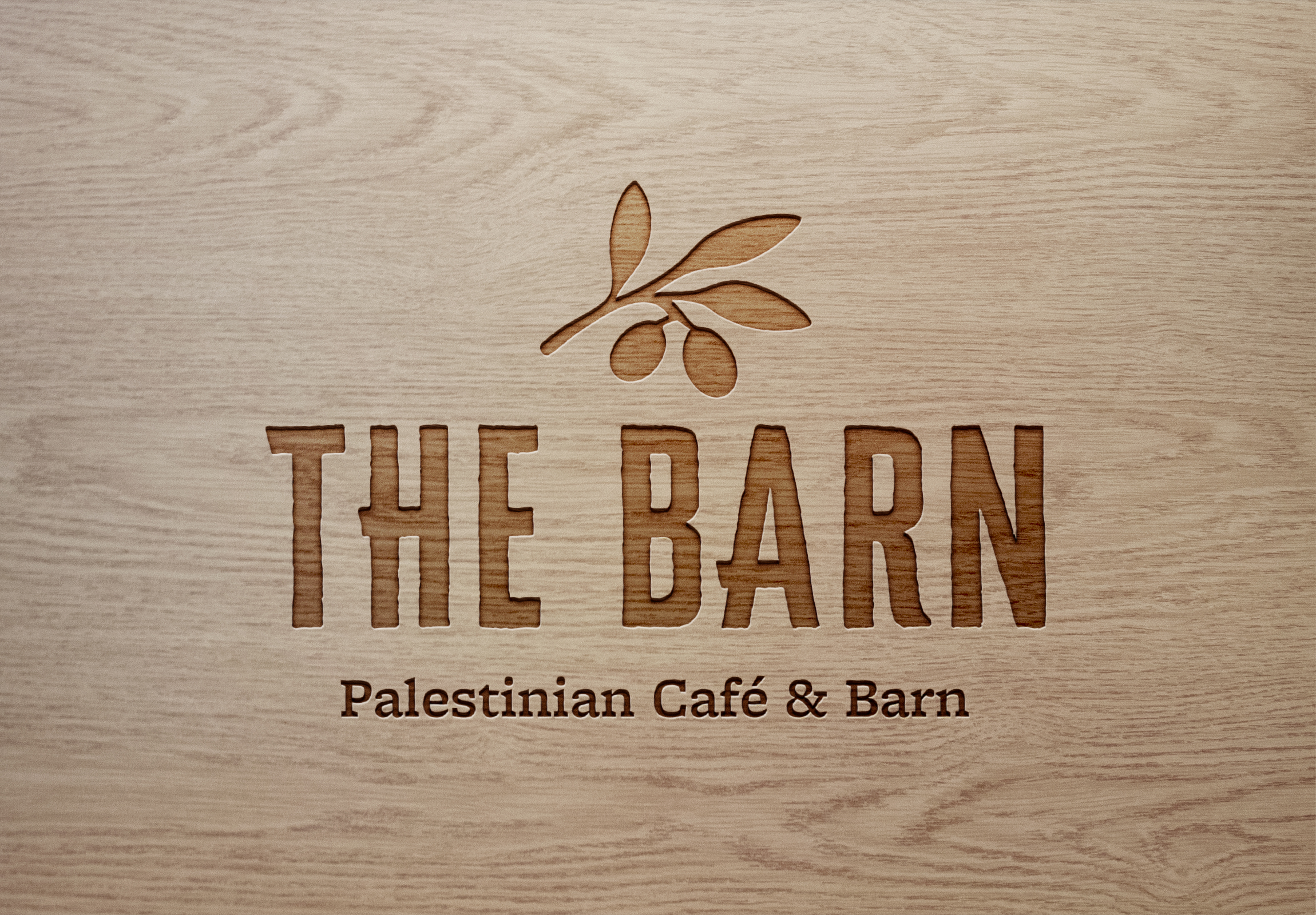 Wooden sign with a leaf and olive branch design, reading 'THE BARN Palestinian Café & Barn' in carved letters.