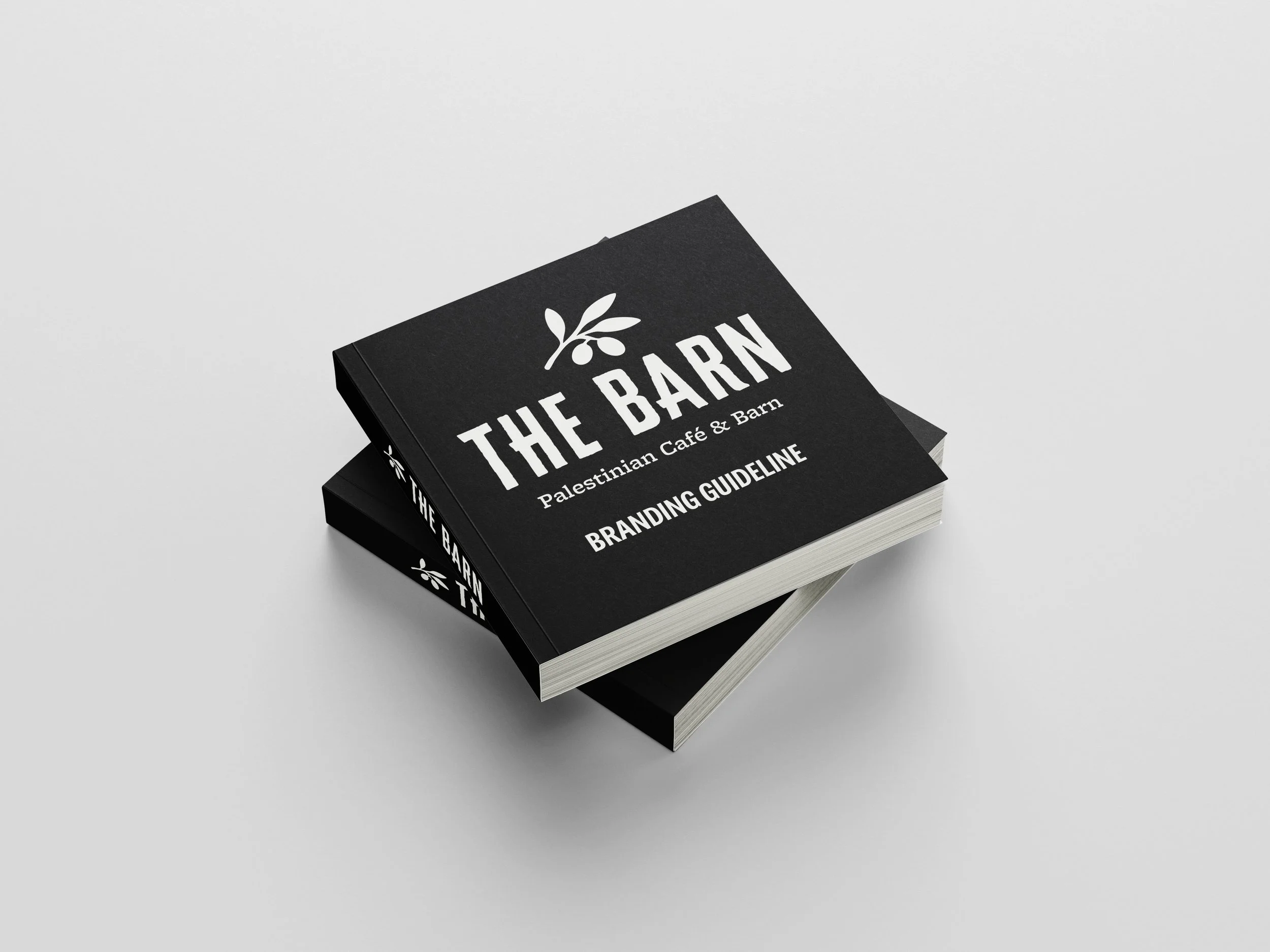 Two black booklets titled 'The Barn: Palestinian Café & Barn Branding Guideline' with white text and a olive leaves logo, placed on a white surface.