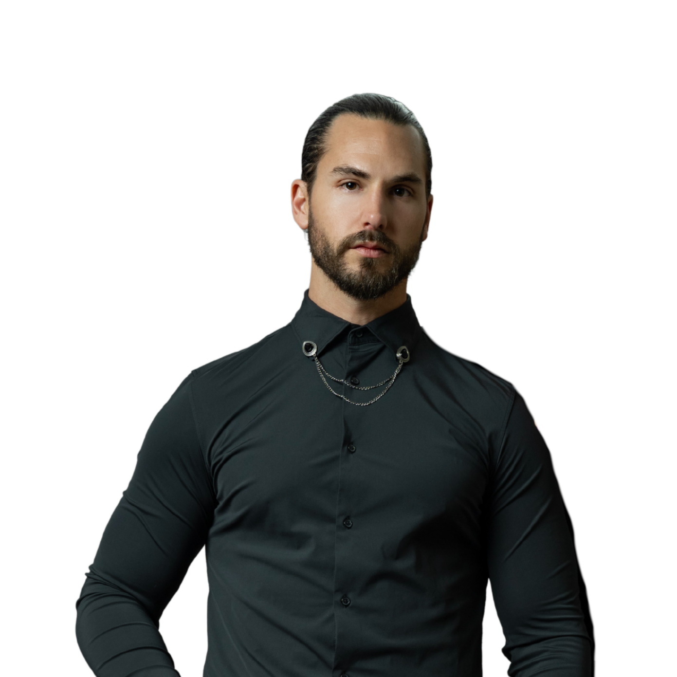 A man with long dark hair, a beard, and a serious expression, wearing a black button-up shirt with chain accessories around the collar, standing against a black background.