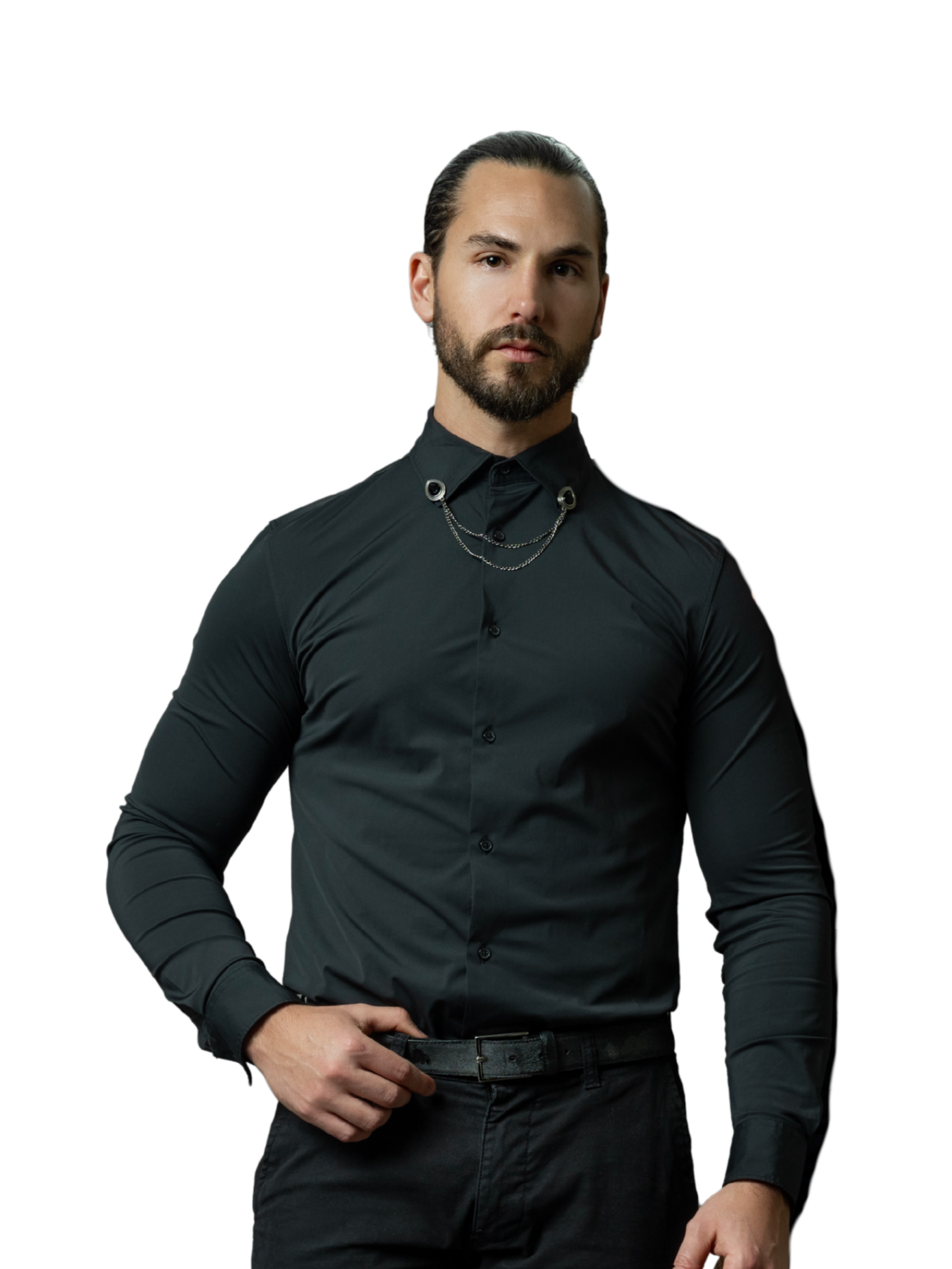 Man with dark hair and beard wearing a black button-up shirt and black pants, standing with one hand on his hip, against a black background.