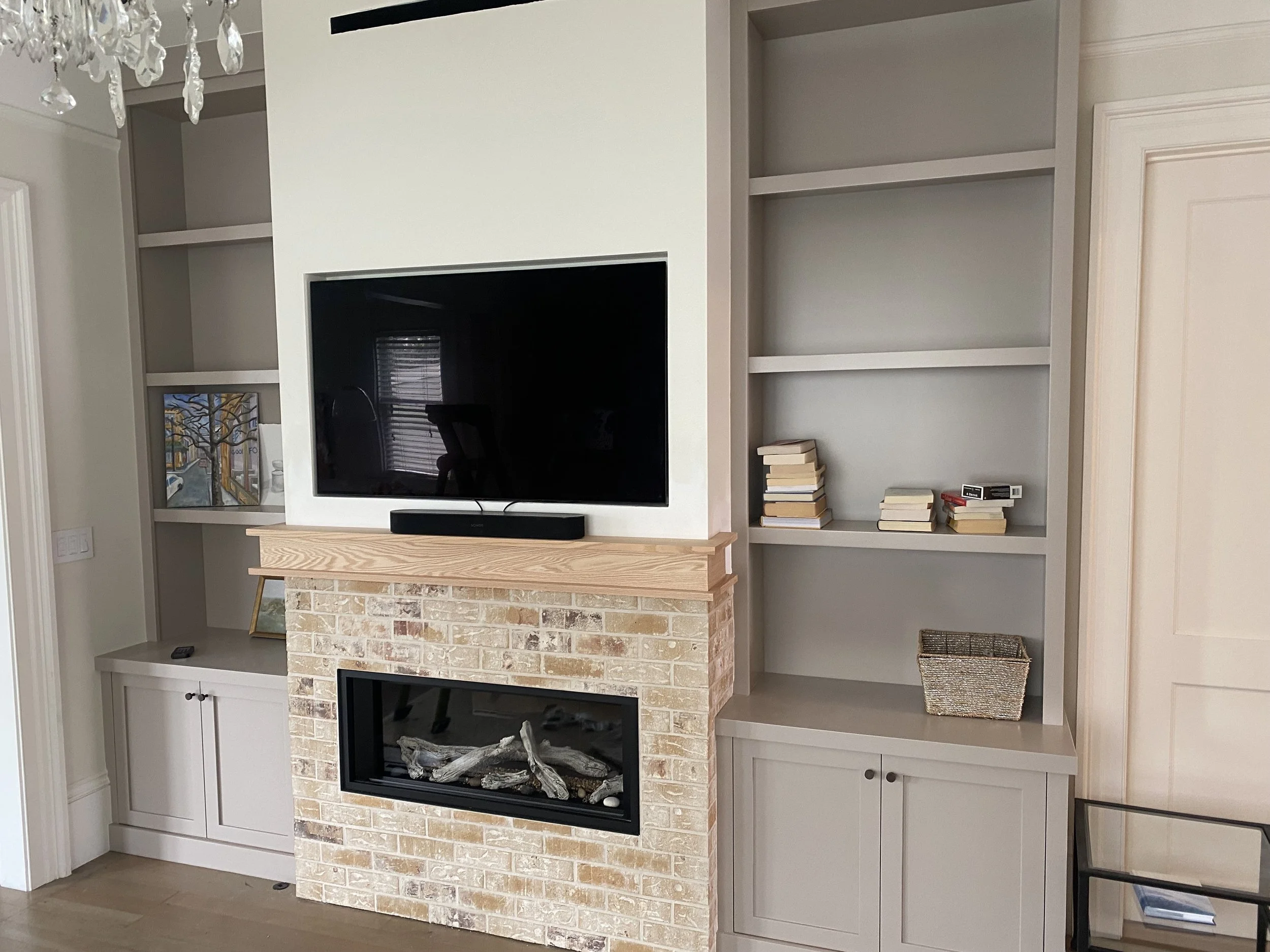 Living room with built-in shelves, a flat-screen TV, a brick fireplace, and decorative items including books and artwork.