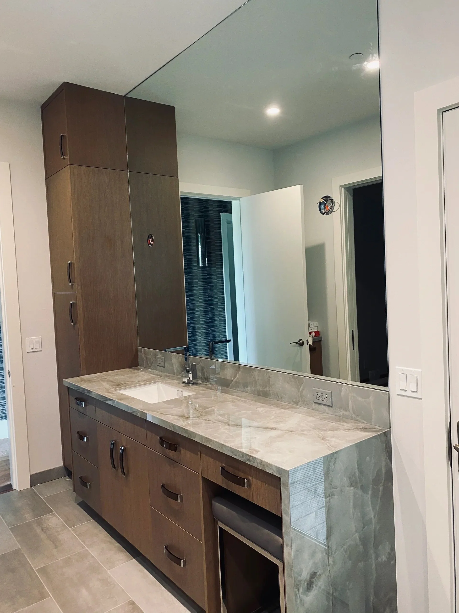 Modern bathroom vanity with wooden cabinets, marble countertop, large mirror, and electrical outlets, in a contemporary bathroom setting.