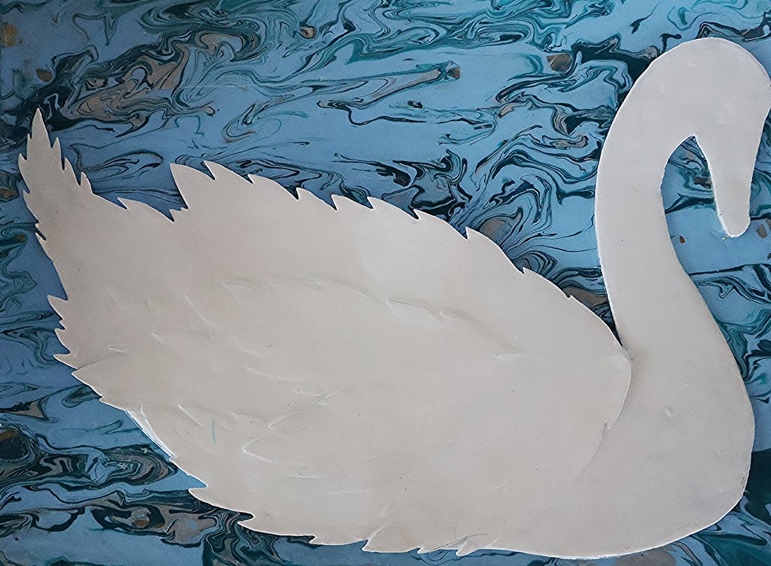 White paper cutout of a swan placed on a marbled blue background.