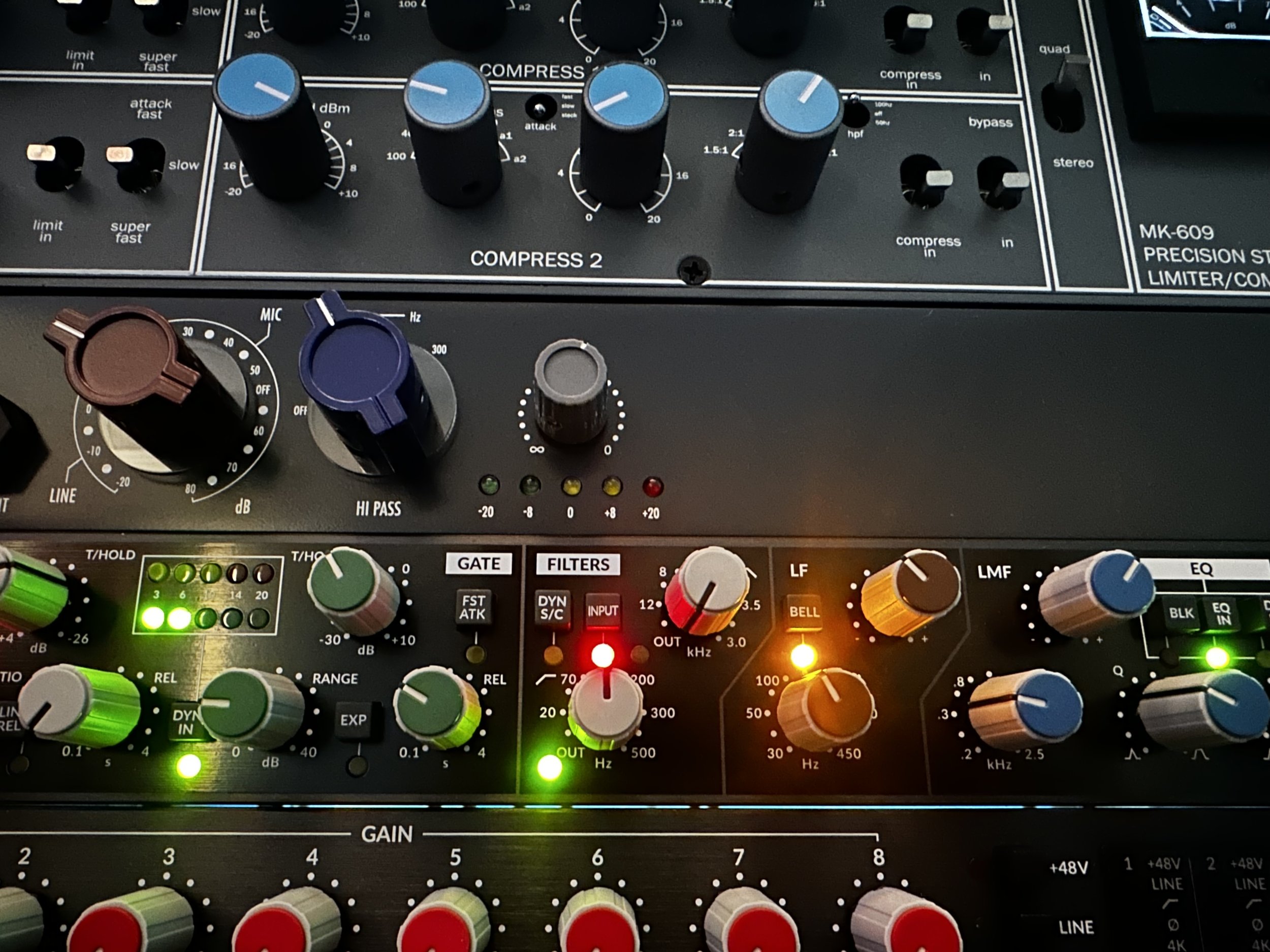 Close-up of a professional audio synthesizer with various knobs and controls, including compressor, equalizer, filters, gain, and LED indicators.