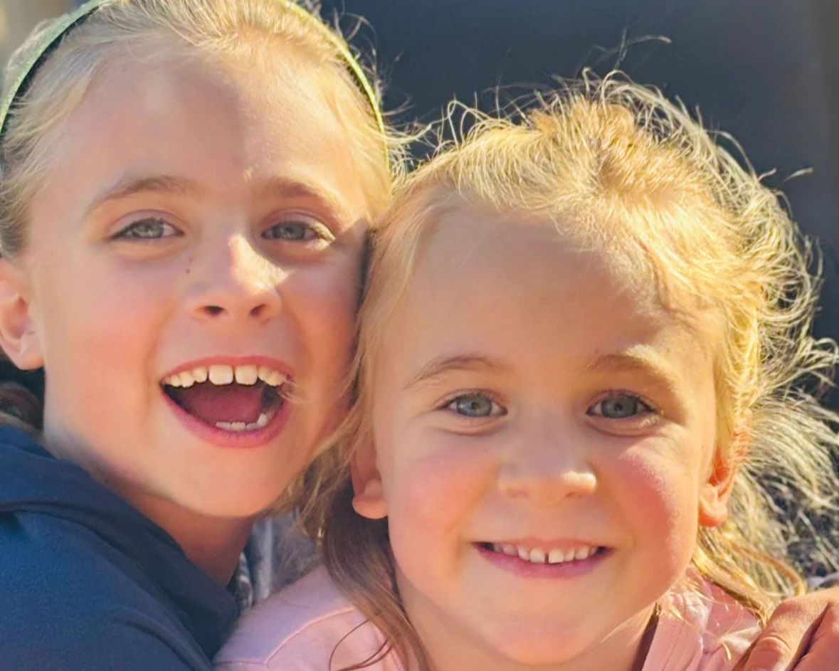 Two children smiling at the camera in the sunshine
