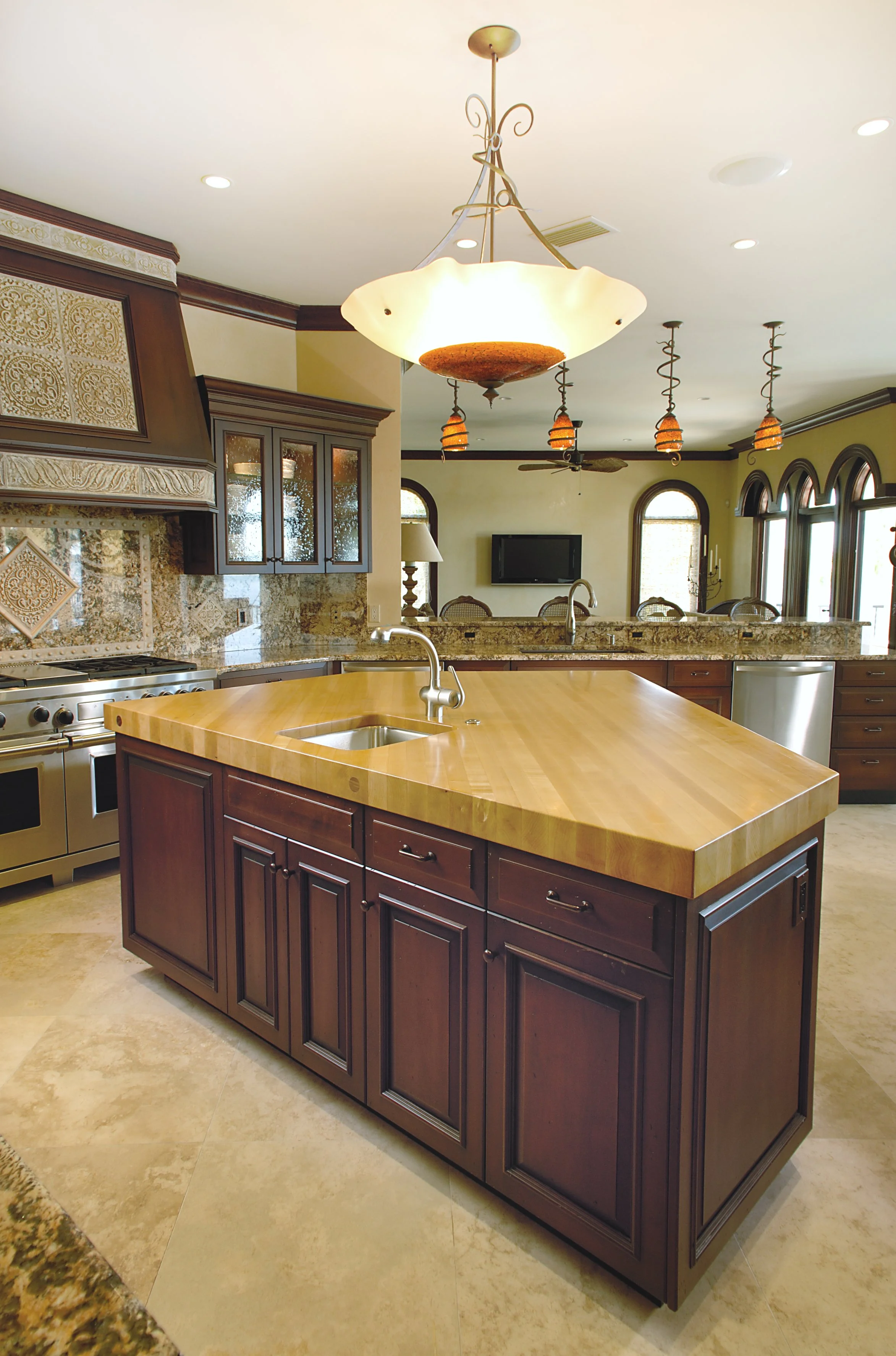 A kitchen with a wooden island, dark wood cabinets, granite countertops, and a decorative light fixture hanging from the ceiling.