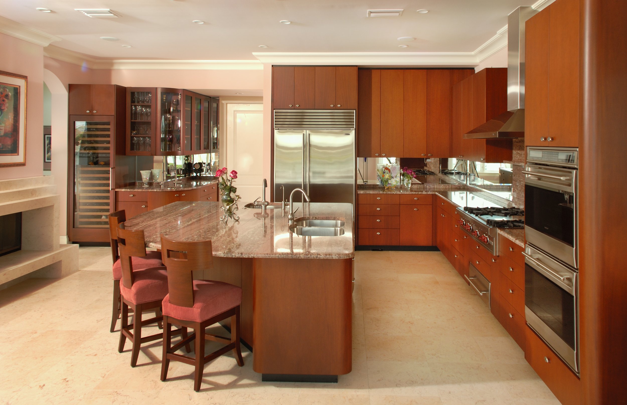 Modern kitchen with wooden cabinets, granite countertops, stainless steel appliances, and a breakfast bar with four pink upholstered chairs.