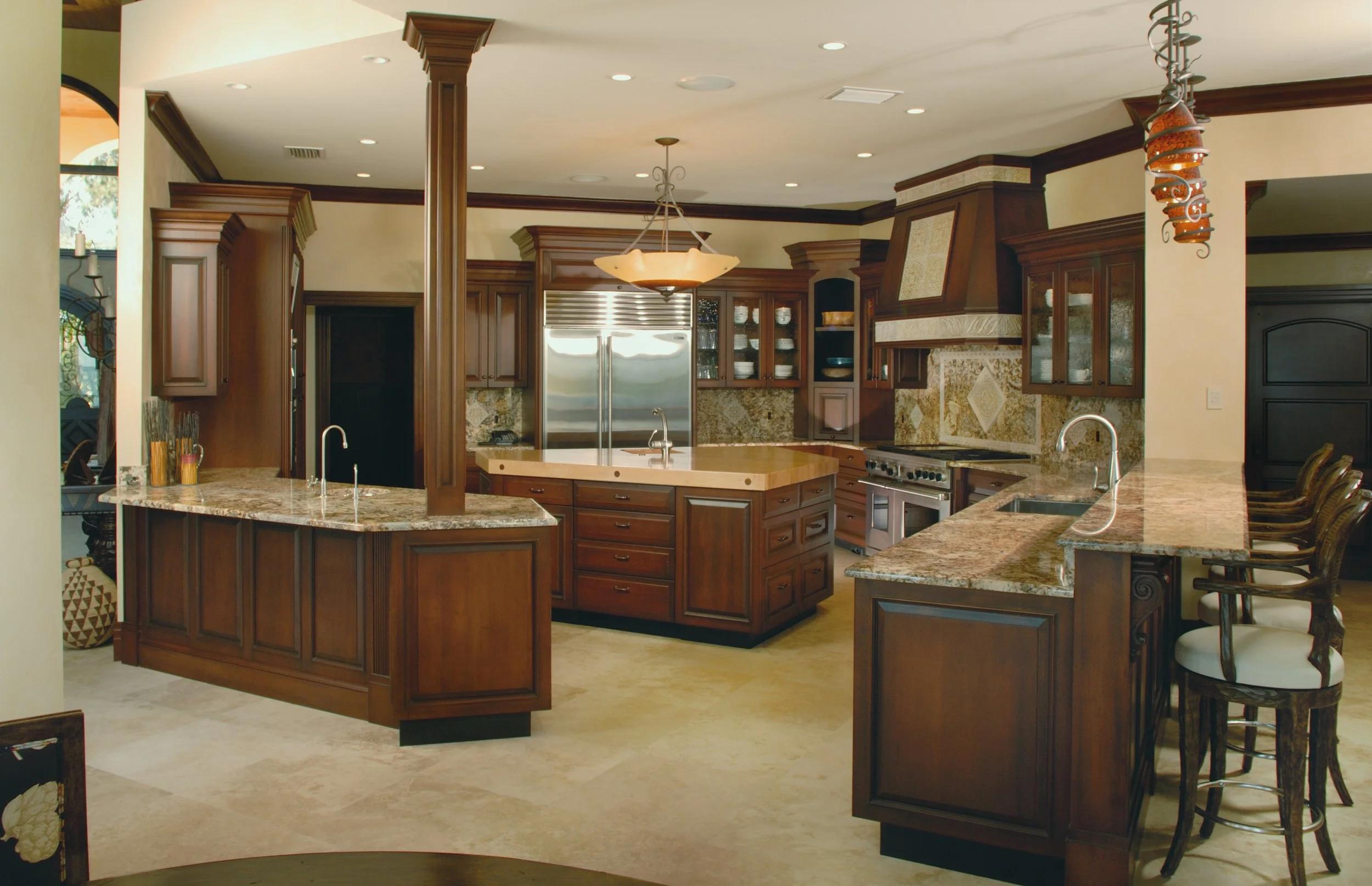 A spacious kitchen with wooden cabinetry, granite countertops, a central island, stainless steel appliances, and a breakfast bar with barstools.