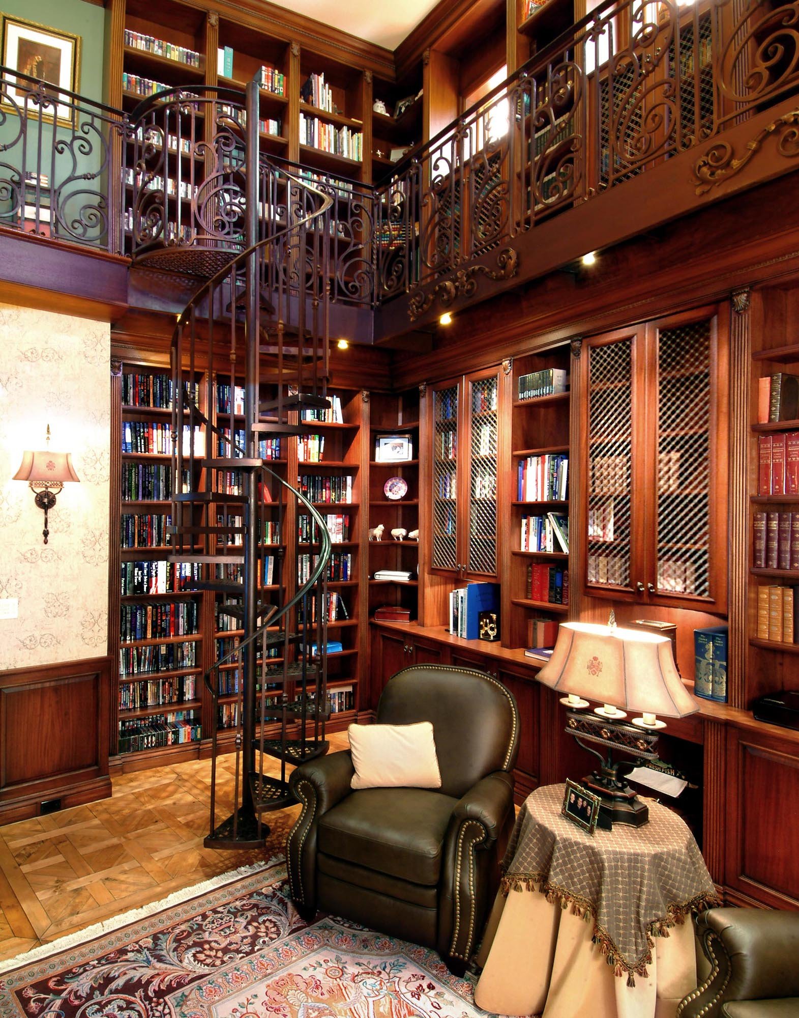 Elegant home library with wooden bookshelves, a spiral staircase, leather armchair, and a side table with a lamp.