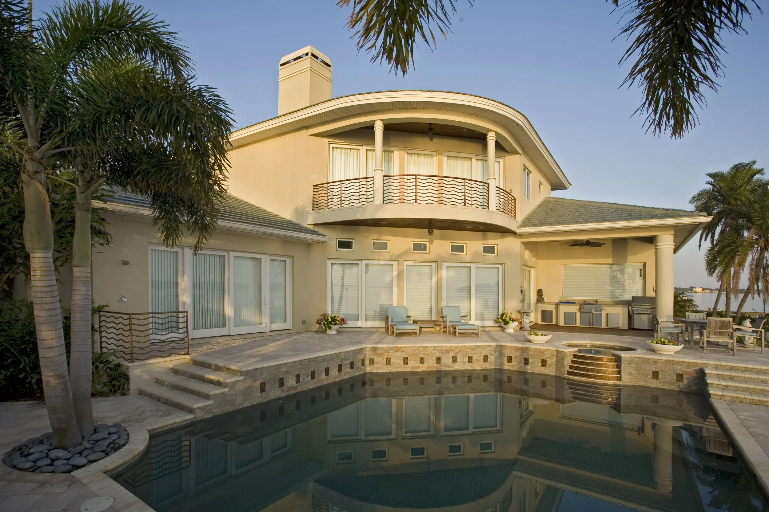 Luxury house with a swimming pool, palm trees, and outdoor seating area at sunset