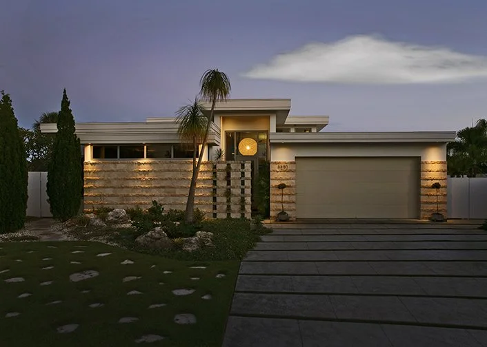 Modern house with a driveway, palm trees, and landscaped front yard at dusk.