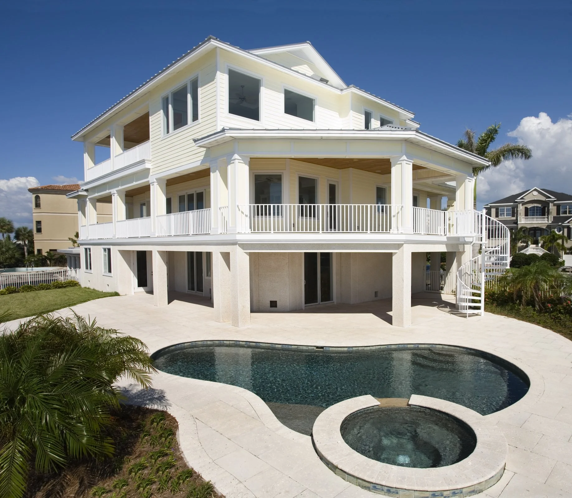 Large white multi-story house with a swimming pool and hot tub in the backyard, surrounded by palm trees and landscaping.