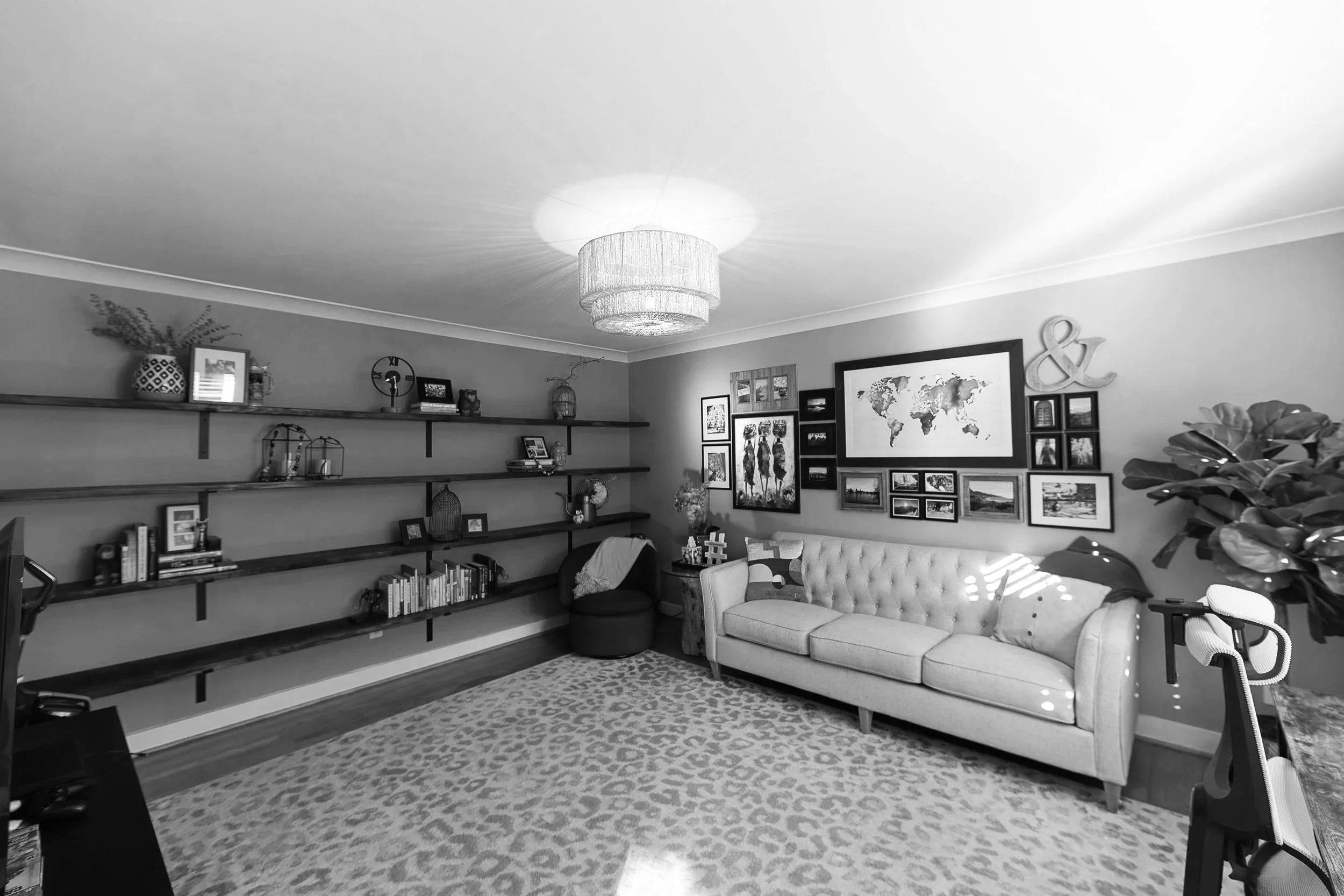 Living room with a beige tufted sofa, framed pictures and artwork, wall shelves with decor, a table with a plant, and a large world map on the wall.