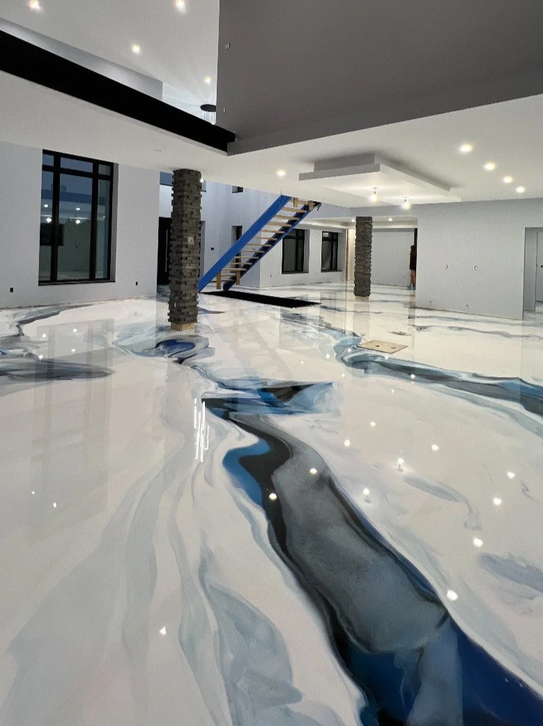 Modern interior with glossy marble floor featuring a blue and black abstract design, white walls, multiple windowed walls, exposed brick columns, a staircase with blue support beams, and recessed lighting.