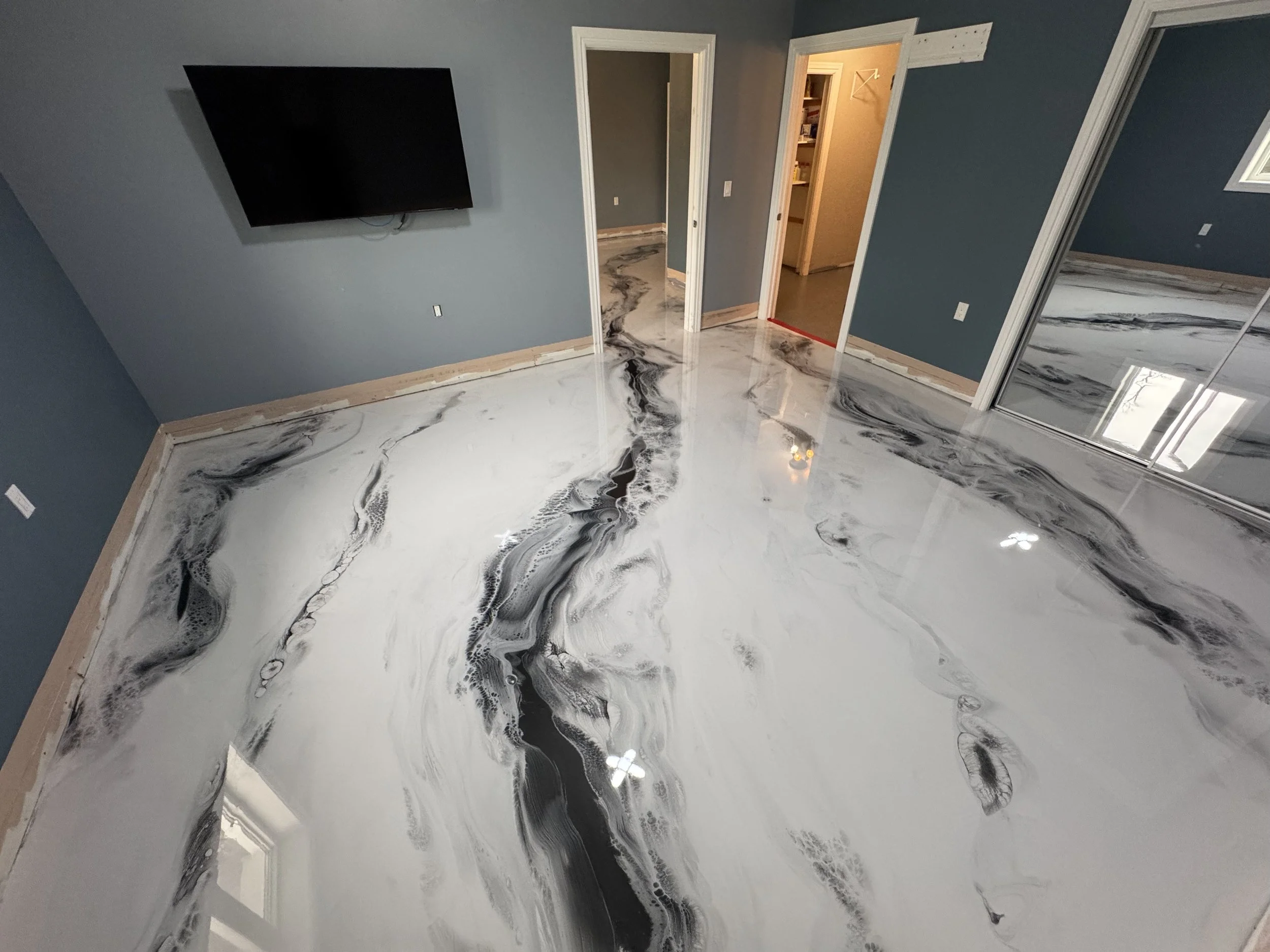 Room with polished marble floor with black and white veining, dark blue walls, a wall-mounted TV, and open doorways leading to other rooms.