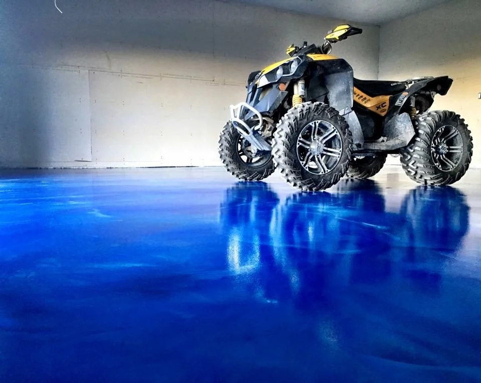 A yellow and black quad bike with large, off-road tires parked on a shiny blue floor inside a dimly lit garage or warehouse.