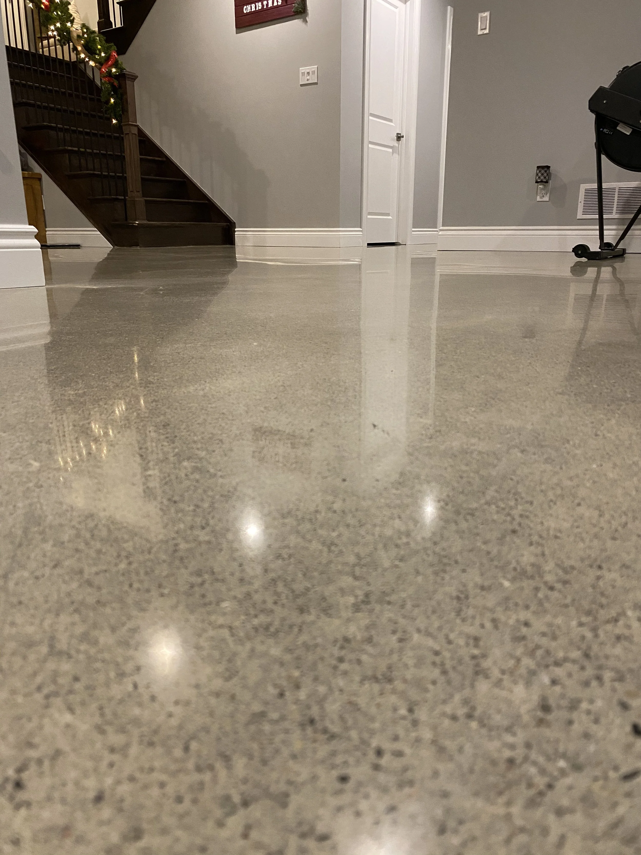 Polished concrete floor in a living room with a staircase decorated with Christmas garland, a door, and a wall with a sign.