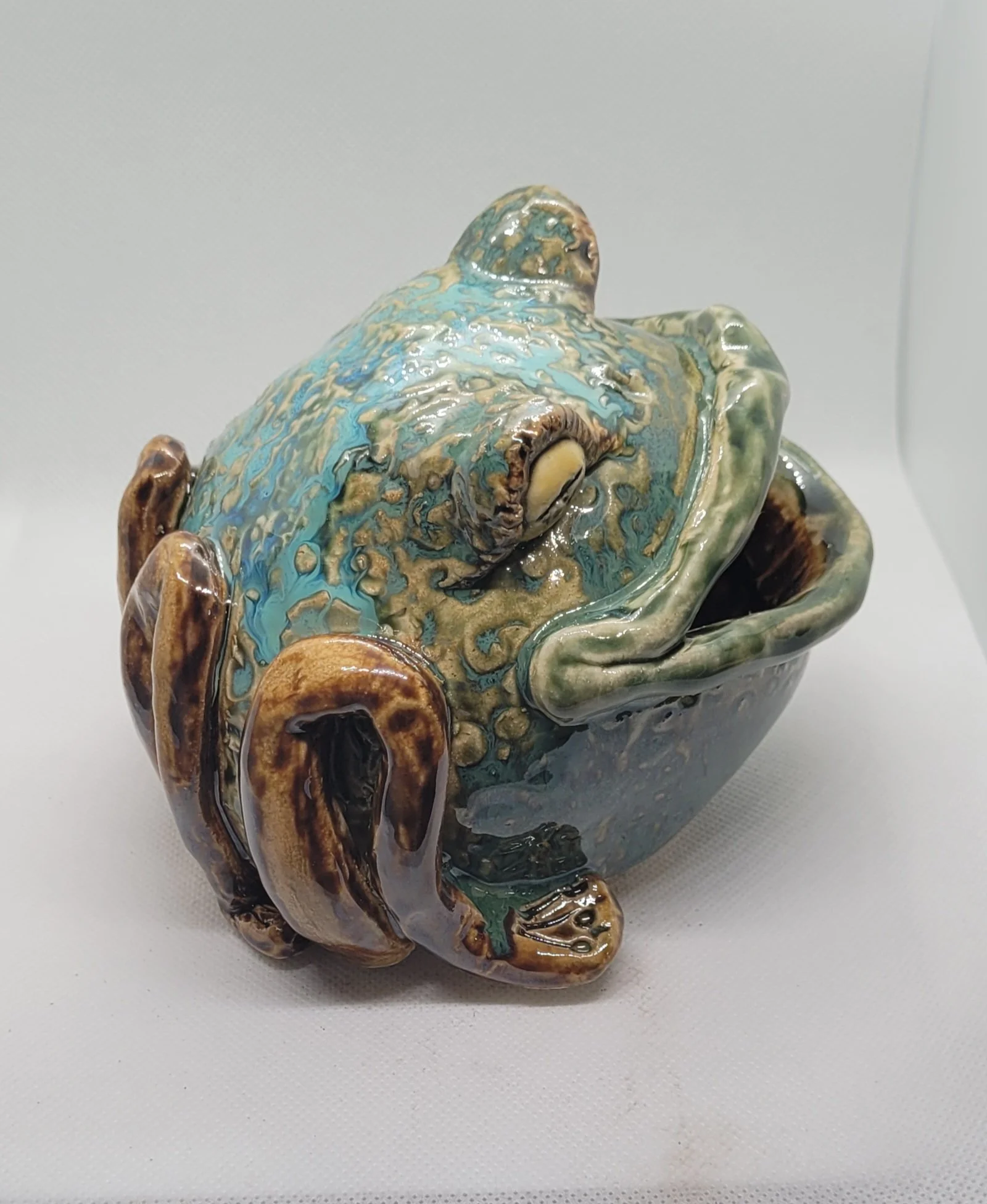 A ceramic frog-shaped dish with a glazed surface in shades of blue, green, and brown, resting on a white background.