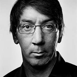 Black and white close-up of a man with glasses and dark hair, looking directly at the camera