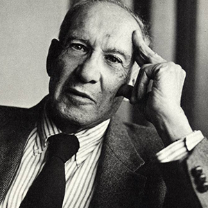 Black and white portrait of a man with a serious expression, wearing a suit and tie, resting his head on his hand.