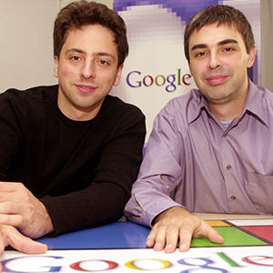 Two men sitting at a table with Google logos in the background.
