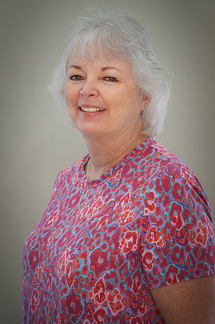 A smiling older woman with short, gray hair wearing a colorful, patterned blouse.