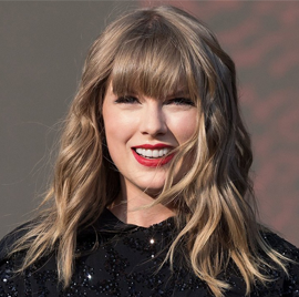 Close-up of a woman with blonde wavy hair and bangs, smiling with visible teeth, wearing a black sparkly top.