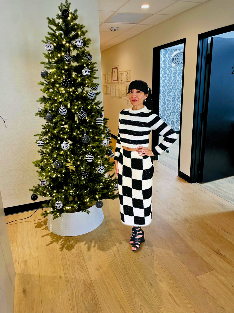 JoviStyle stands beside a decorated Christmas tree with black, white, and silver ornaments, wearing a black and white checkered outfit in a brightly lit room.