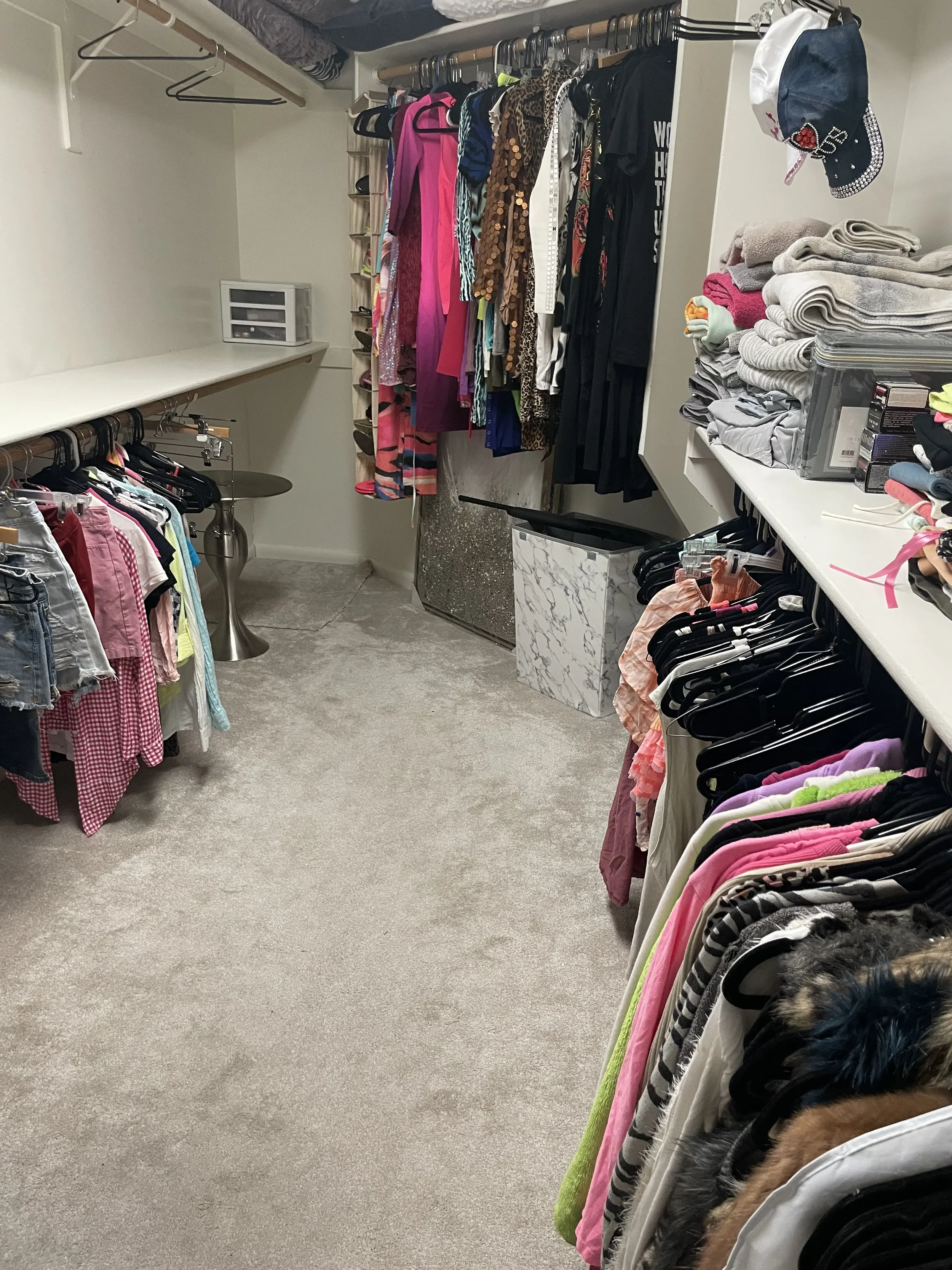 A walk-in closet with clothing on racks and shelves, including casual, formal, and children's clothes, with some accessories and storage boxes.