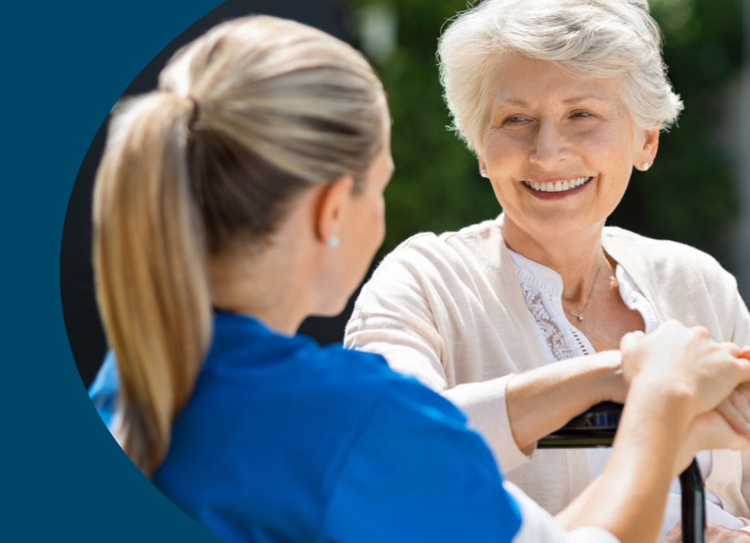 An elderly woman smiling while sitting on a park bench and talking to a caregiver or family member.