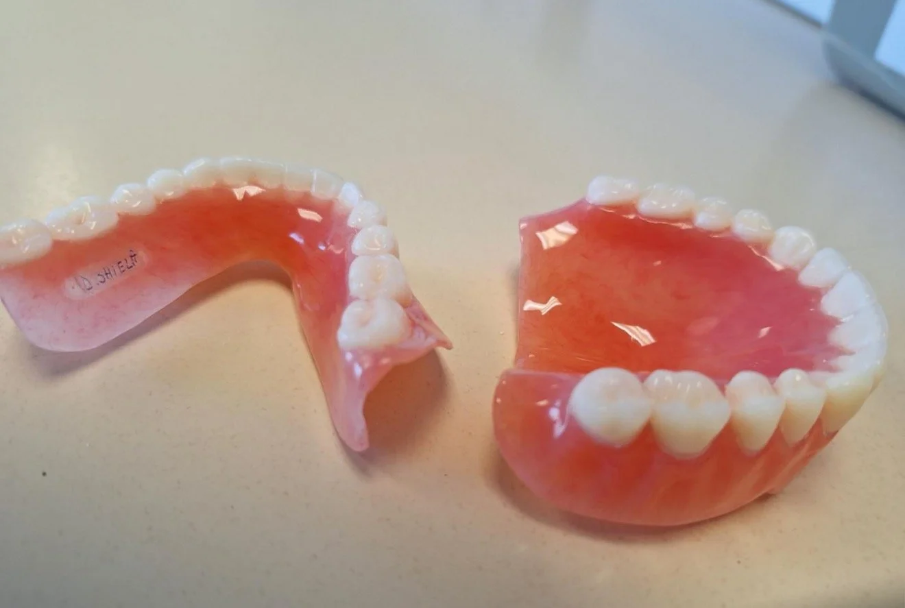 Two sets of pink and white dentures, one partial and the other full, placed on a light-colored surface.