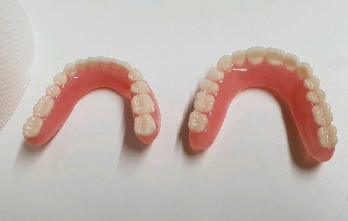 Two sets of artificial dentures on a white surface, each with pink gums and white teeth.
