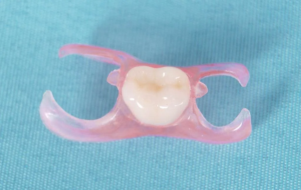 A clear dental appliance with a white tooth model in the center, laid on a teal fabric background.