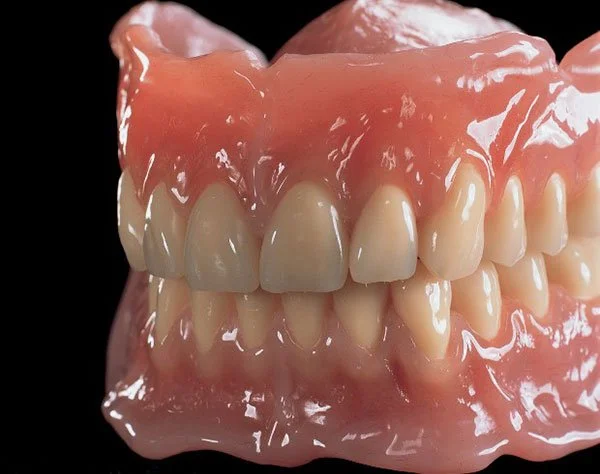 A set of dentures with a pink acrylic base and white artificial teeth, showing the upper and lower arches.