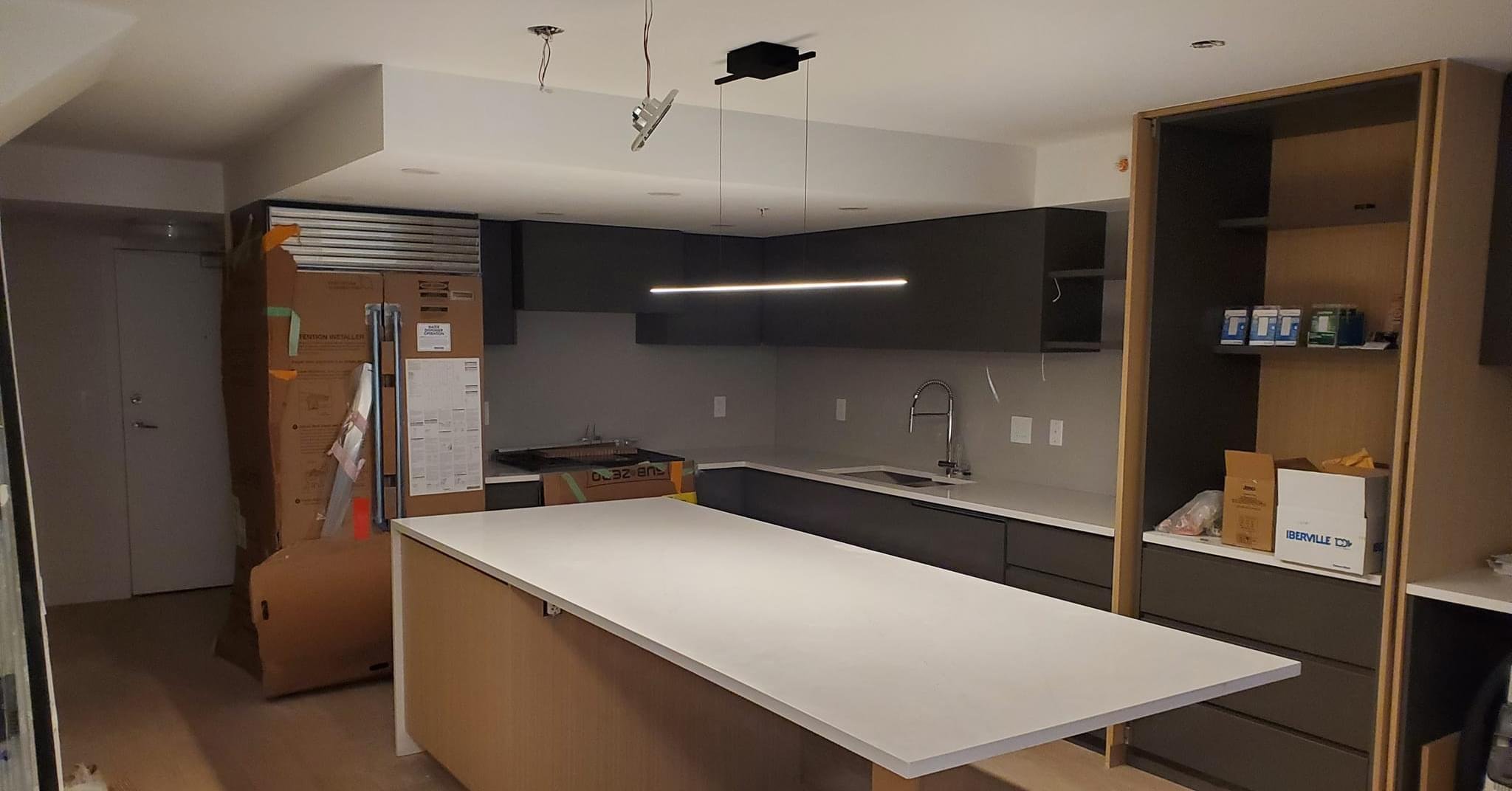 Modern kitchen with black cabinets and a white island countertop, some items still unpacked, suggesting ongoing installation or renovation.