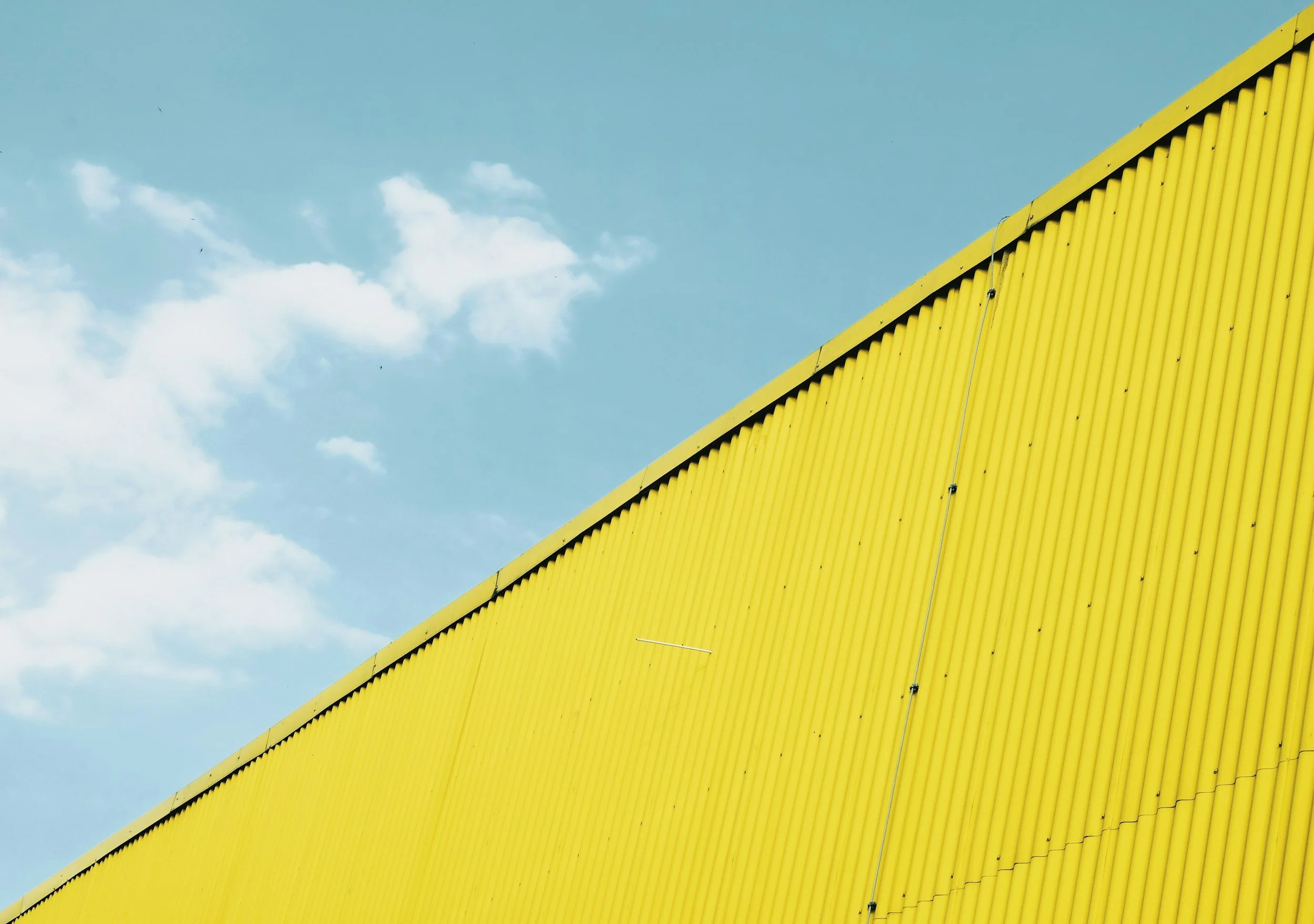 Vista del techo de un edificio amarillo con cielo azul y nubes blancas en el fondo.
