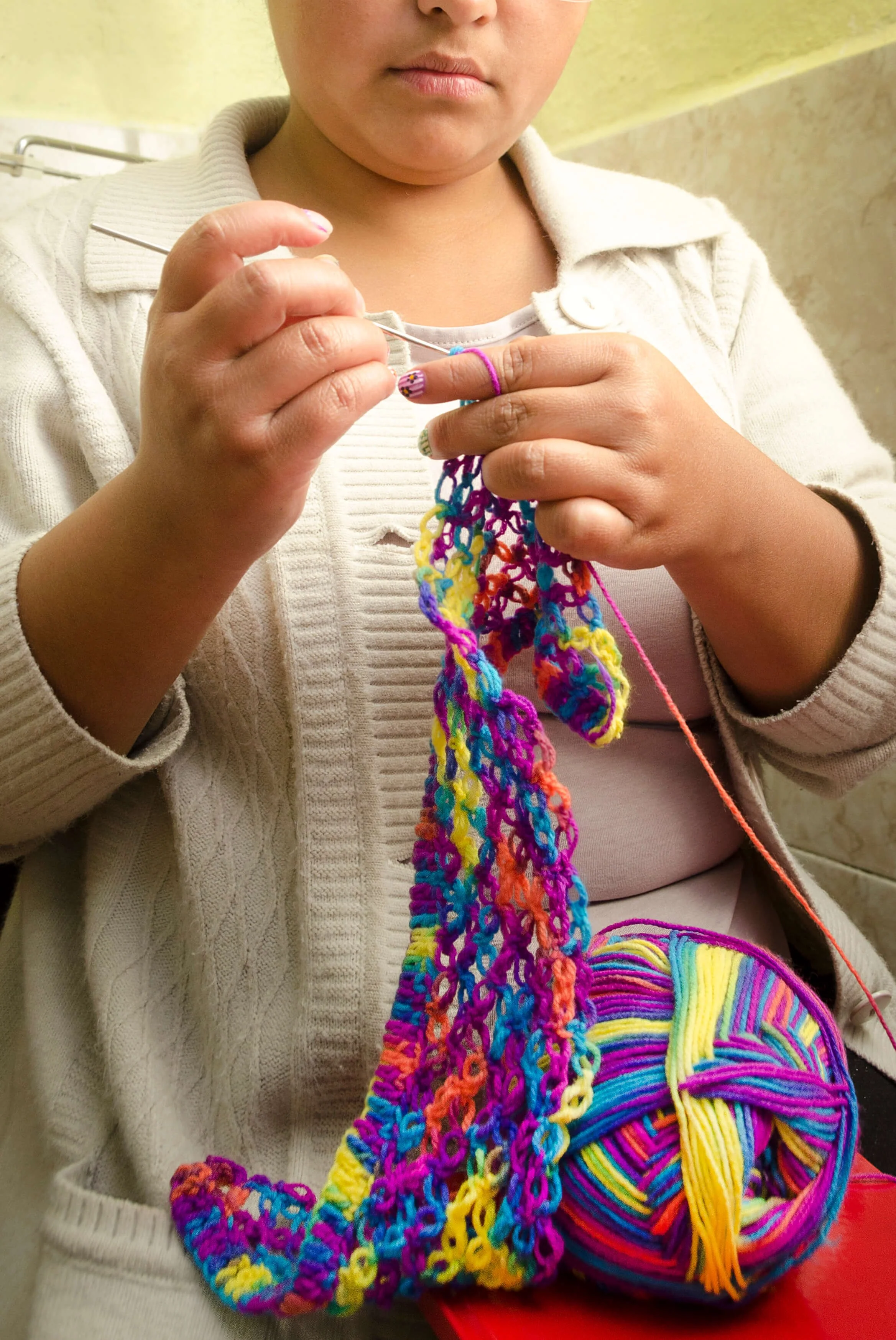 Persona haciendo punto con lana de colores en un lugar cerrado.