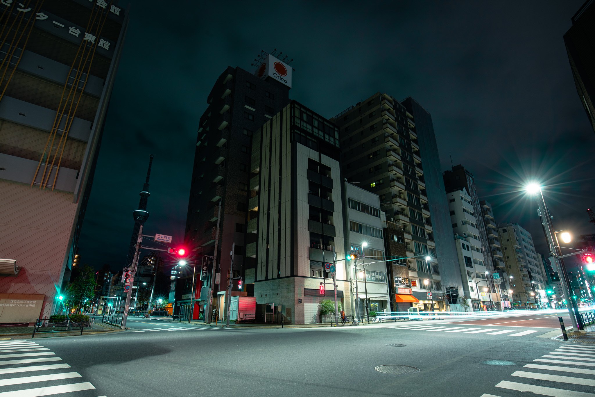 Nighttime city street with tall buildings, illuminated traffic lights, and long exposure light streaks from passing vehicles.