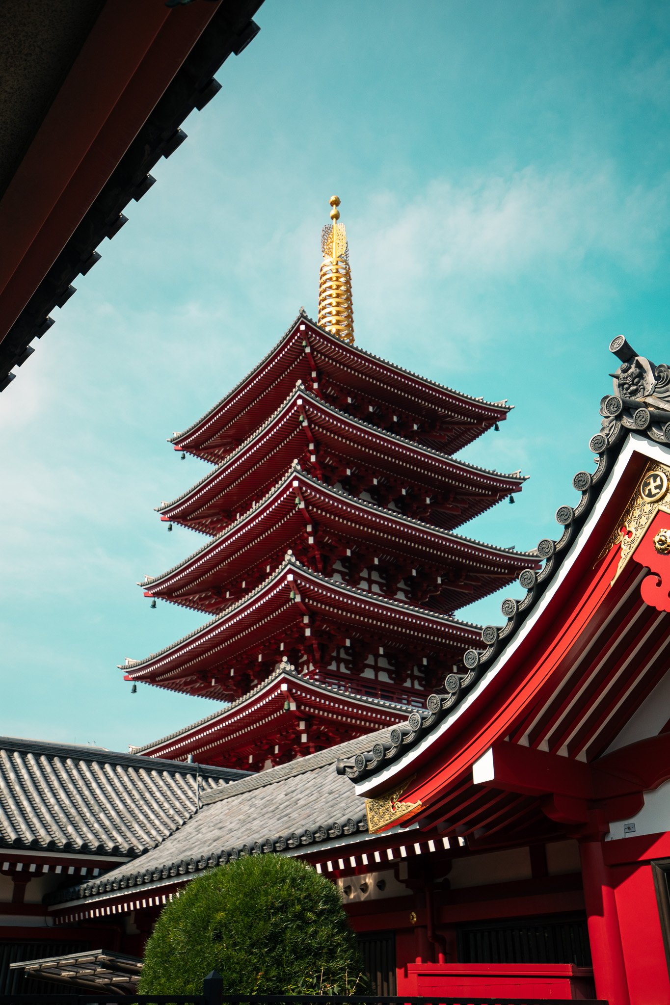 A multi-tiered red pagoda with a golden spire on top, traditional Japanese temple architecture, set against a blue sky.