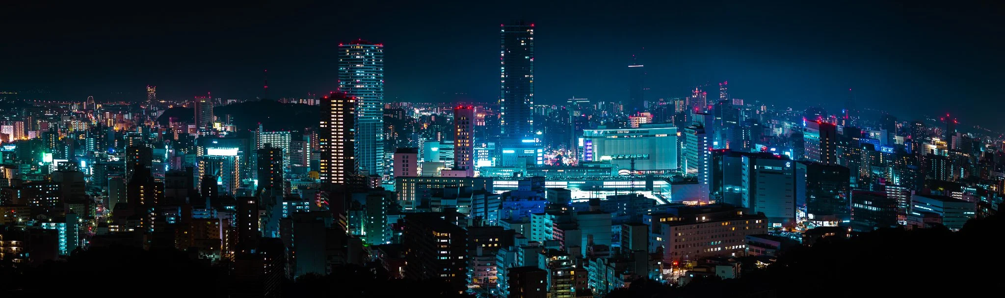Nighttime cityscape of a brightly lit urban area with numerous skyscrapers and high-rise buildings.