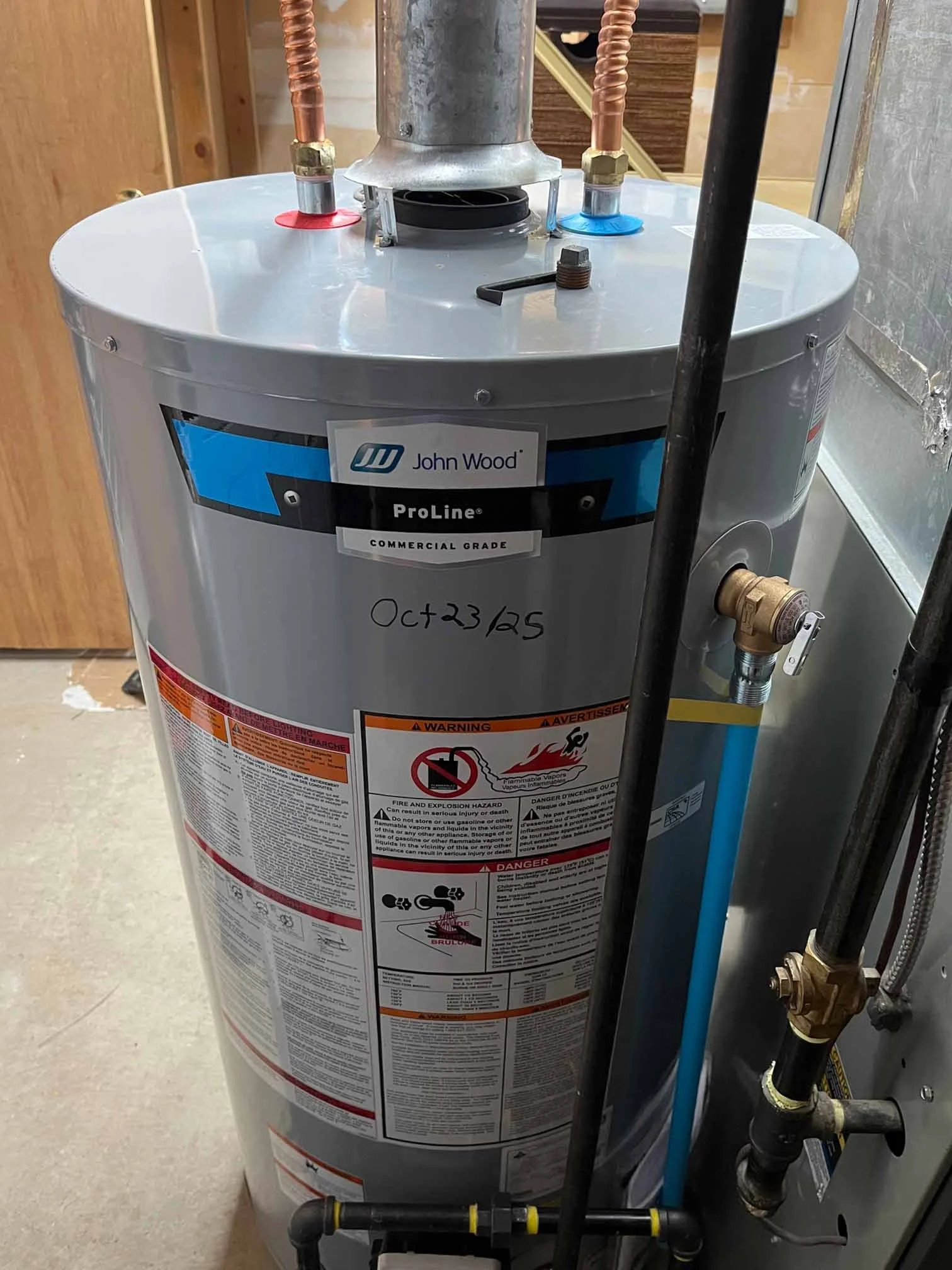 A boiler with pipes and labels, including a sticker with the date October 23, 2025, in a building utility area.